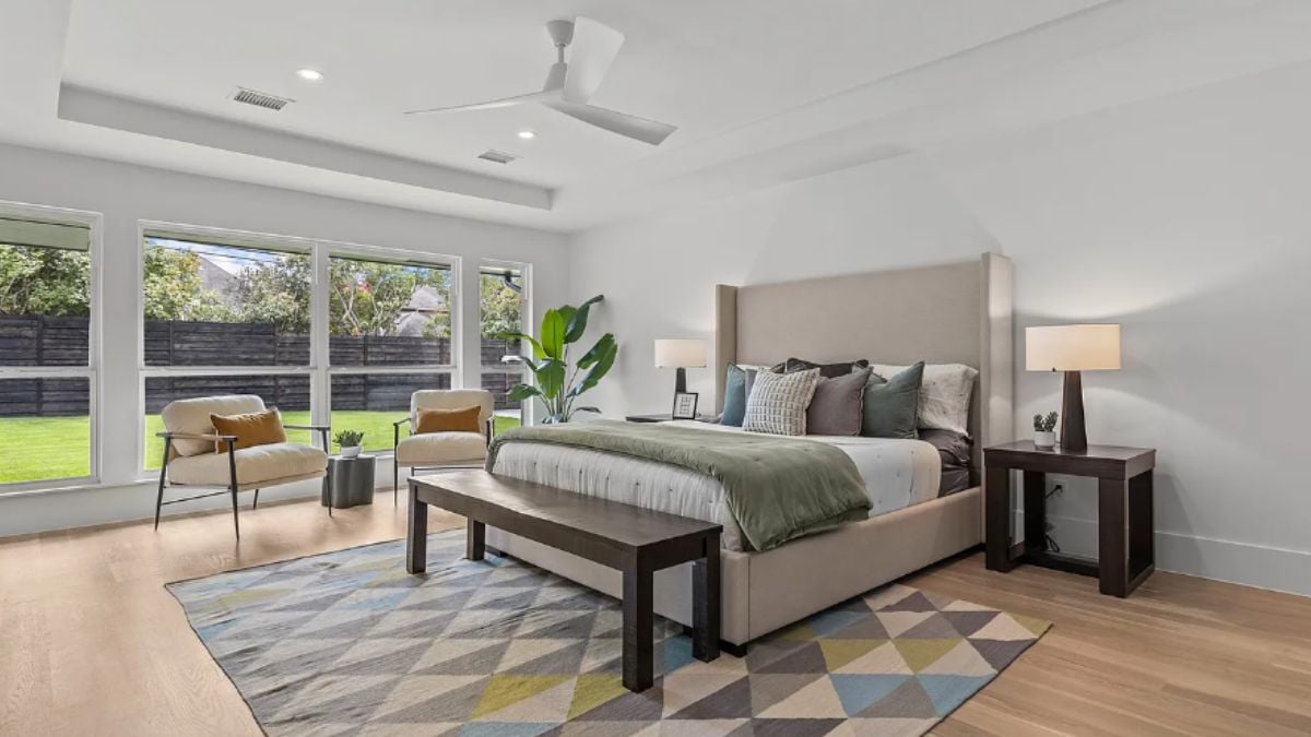 A bedroom with a bed, windows, a ceiling fan, a rug, chairs, nightstands, and a bench.