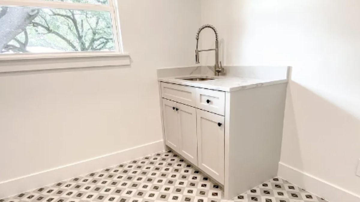 A laundry room with a cabinet, a sink, and a window.