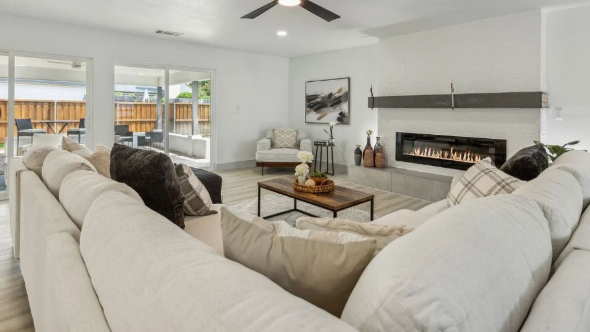 A living room with a fireplace, a painting, a ceiling fan, couches with pillows, and a center table.