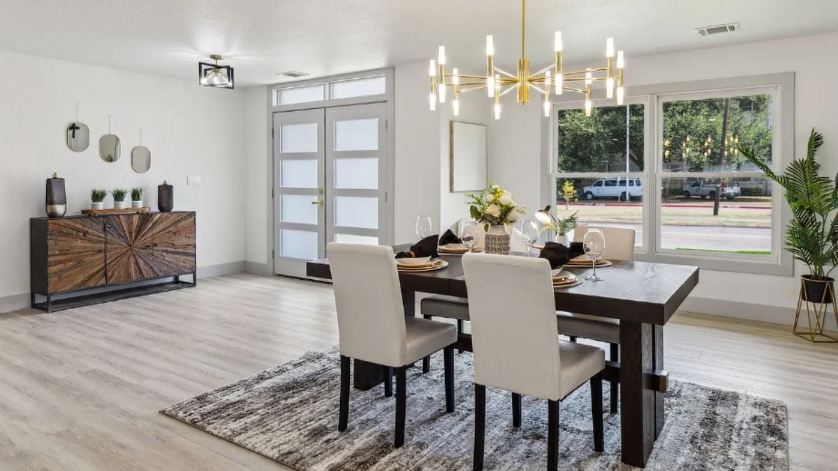 A dining room with a chandelier, a rug, a cabinet, and a dining table surrounded by chairs.