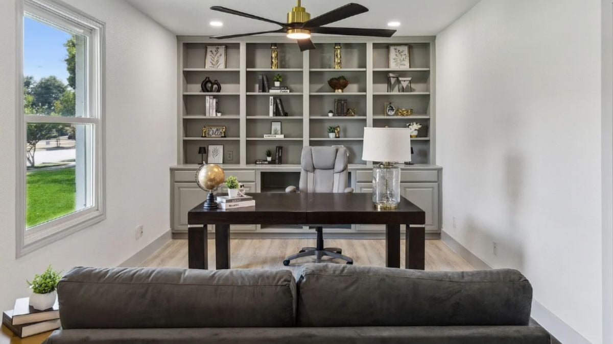 A home office with a shelf, a window, a couch, and a desk with an office chair.