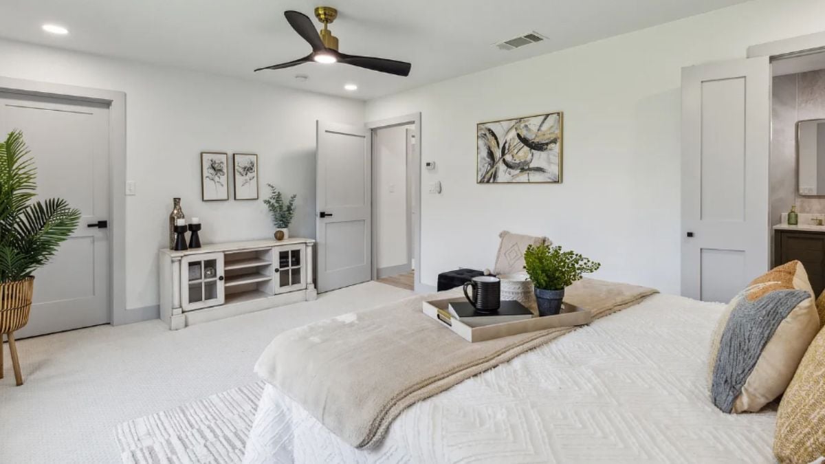 A bedroom with a bed, a ceiling fan, paintings, and a cabinet.