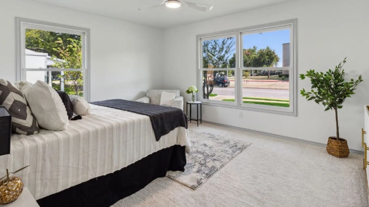 A bedroom with windows, a rug, a bed, a houseplant, and a single couch.
