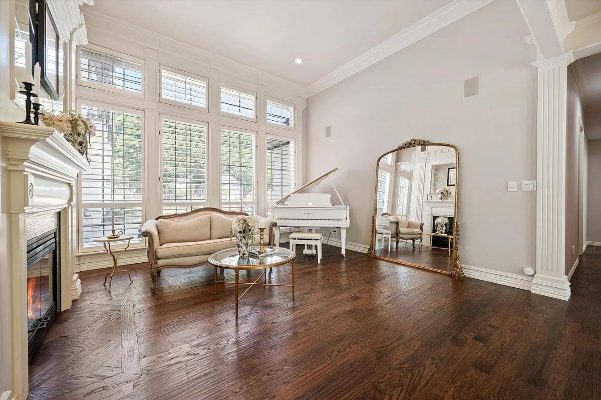 Living room with a baby grand piano, a traditional sofa, a large arched mirror, and a fireplace.
