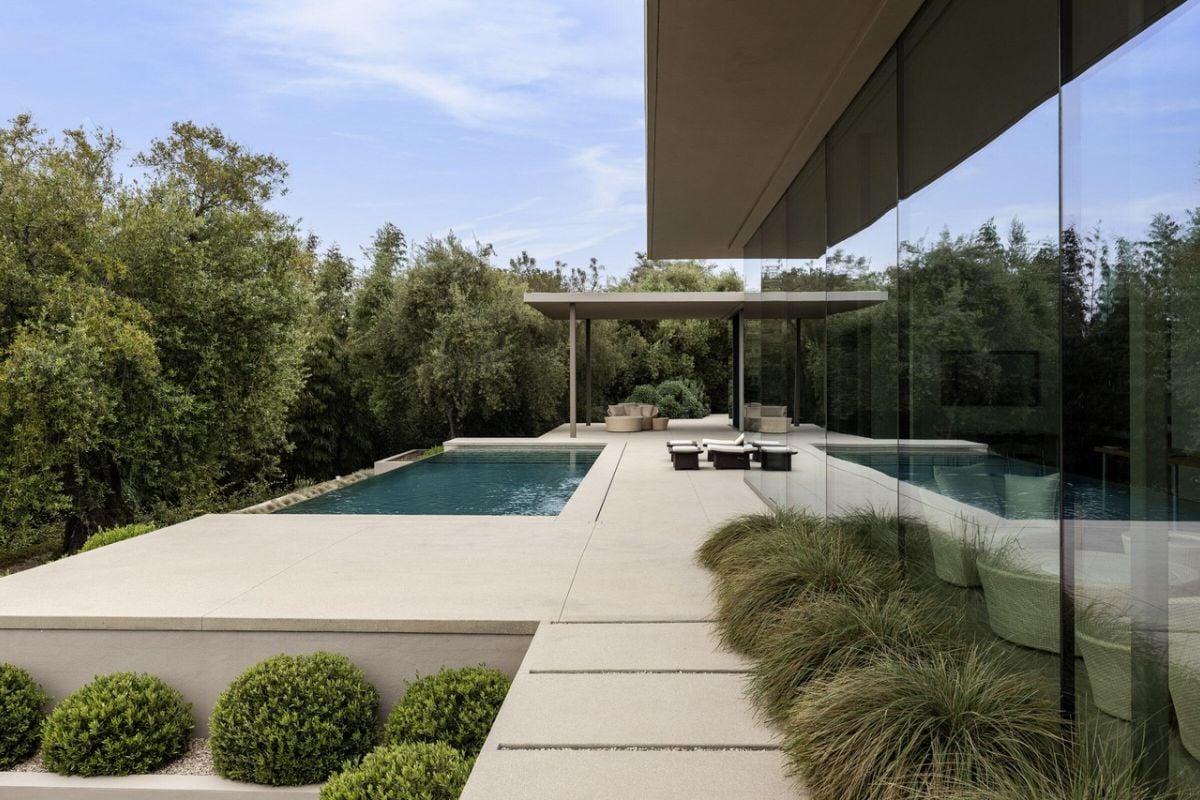 A swimming pool with trees, plants, and chairs on the poolside.