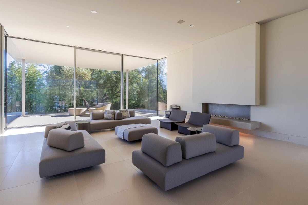 A living room with floor-to-ceiling windows, gray couches, chairs, and an ottoman.