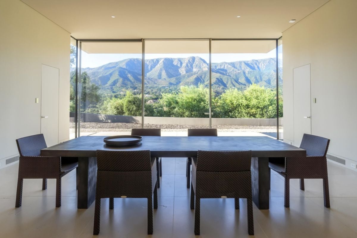 A dining room with floor-to-ceiling windows and a long table surrounded by chairs.
