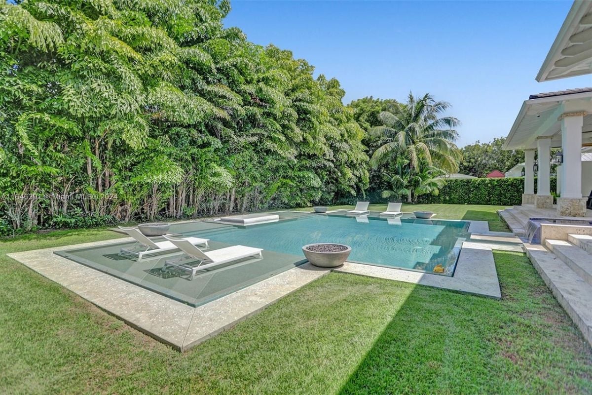 A swimming pool with comfy chairs, surrounded by trees.