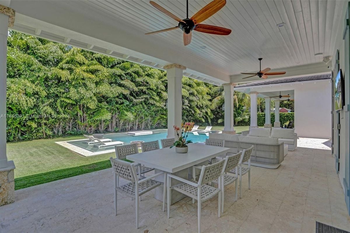 A porch with ceiling fans, a dining table surrounded by chairs, and couches.