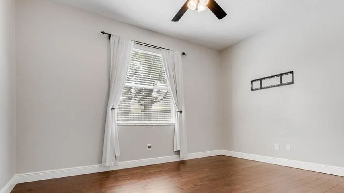 A bedroom with a ceiling fan, wooden floor and a window.