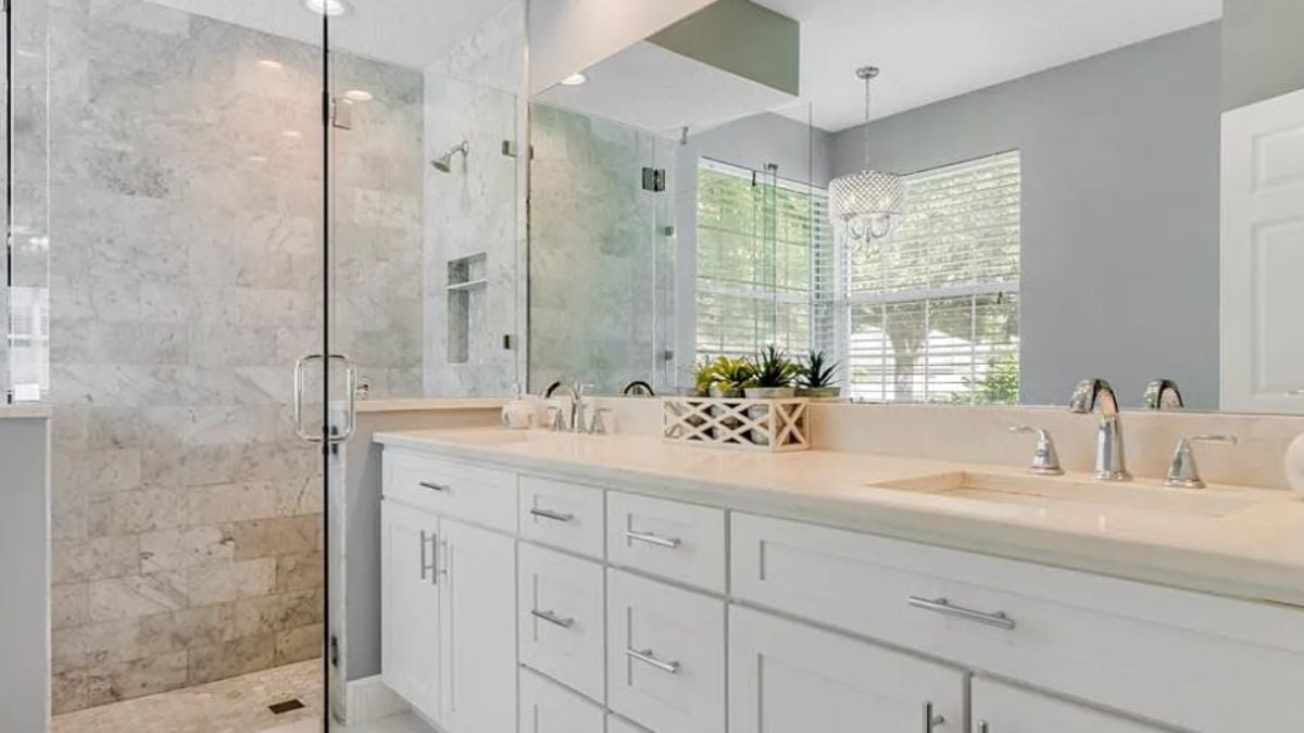 A bathroom with a dual vanity, a mirror, a cabinet, and a shower room.
