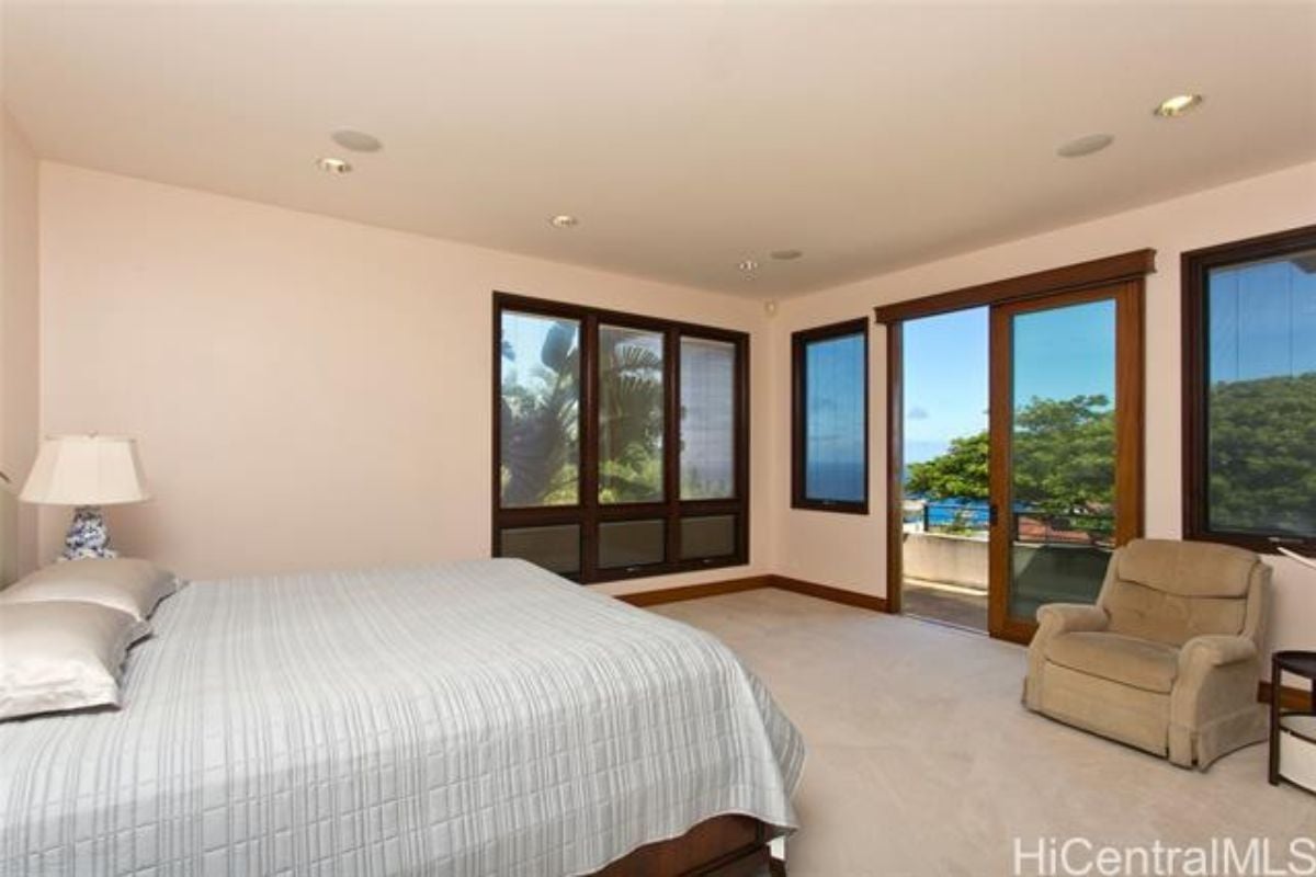 A bedroom with a bed, chair, and windows.