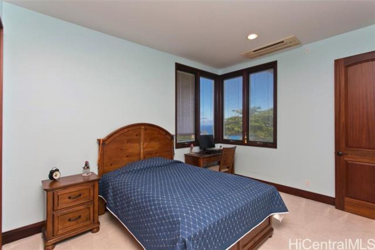 A bedroom with a bed, windows, a nightstand, and a desk with a chair.