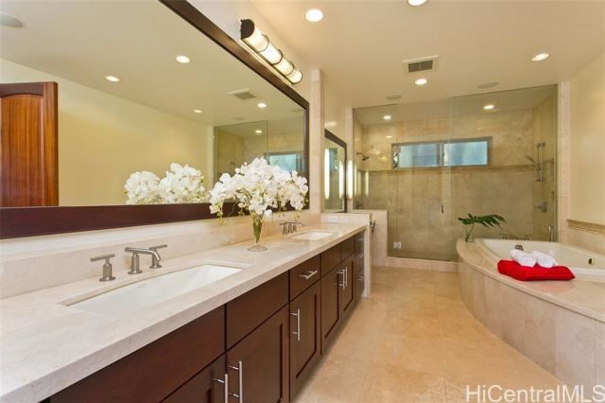 A bathroom with a dual vanity, mirror, bathtub, and cabinet.