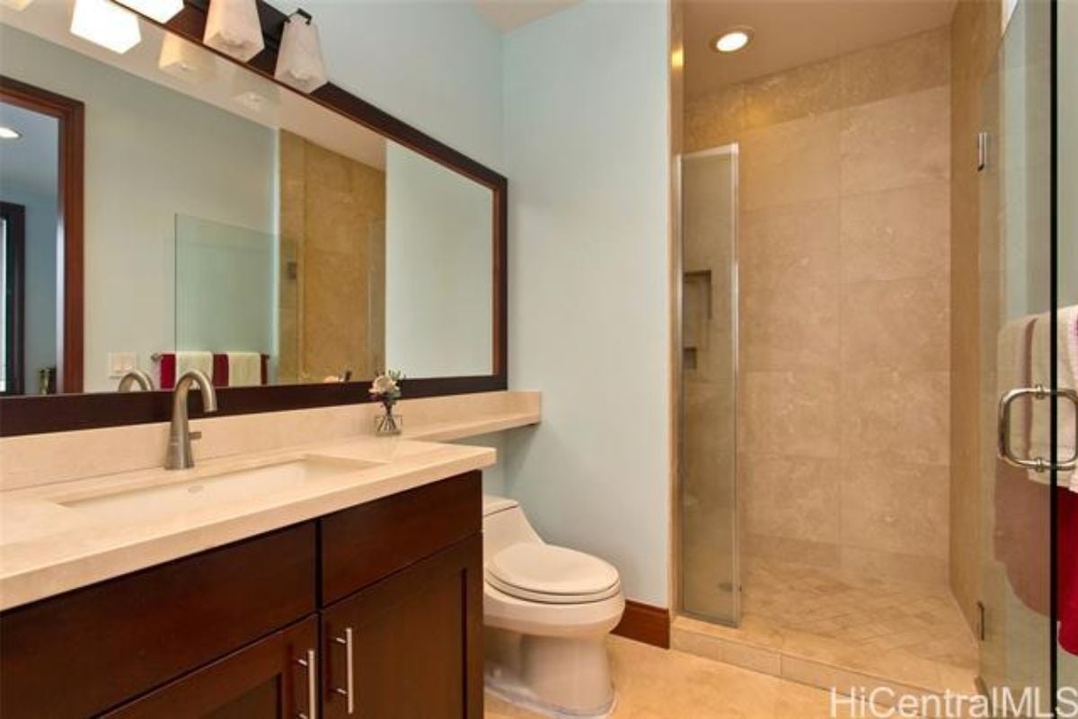 A bathroom with a vanity, mirror, toilet, and shower room.
