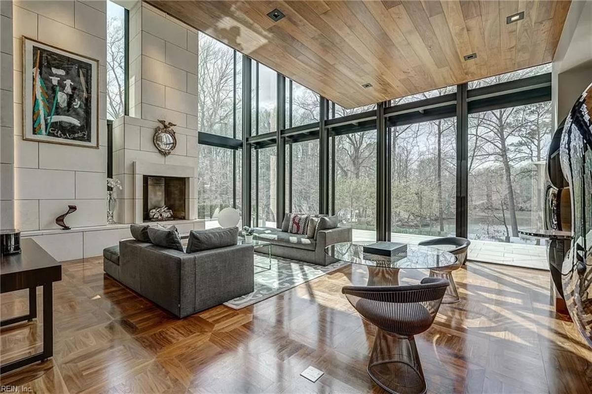 Living room with couches, a fireplace, glass walls and hardwood floors.
