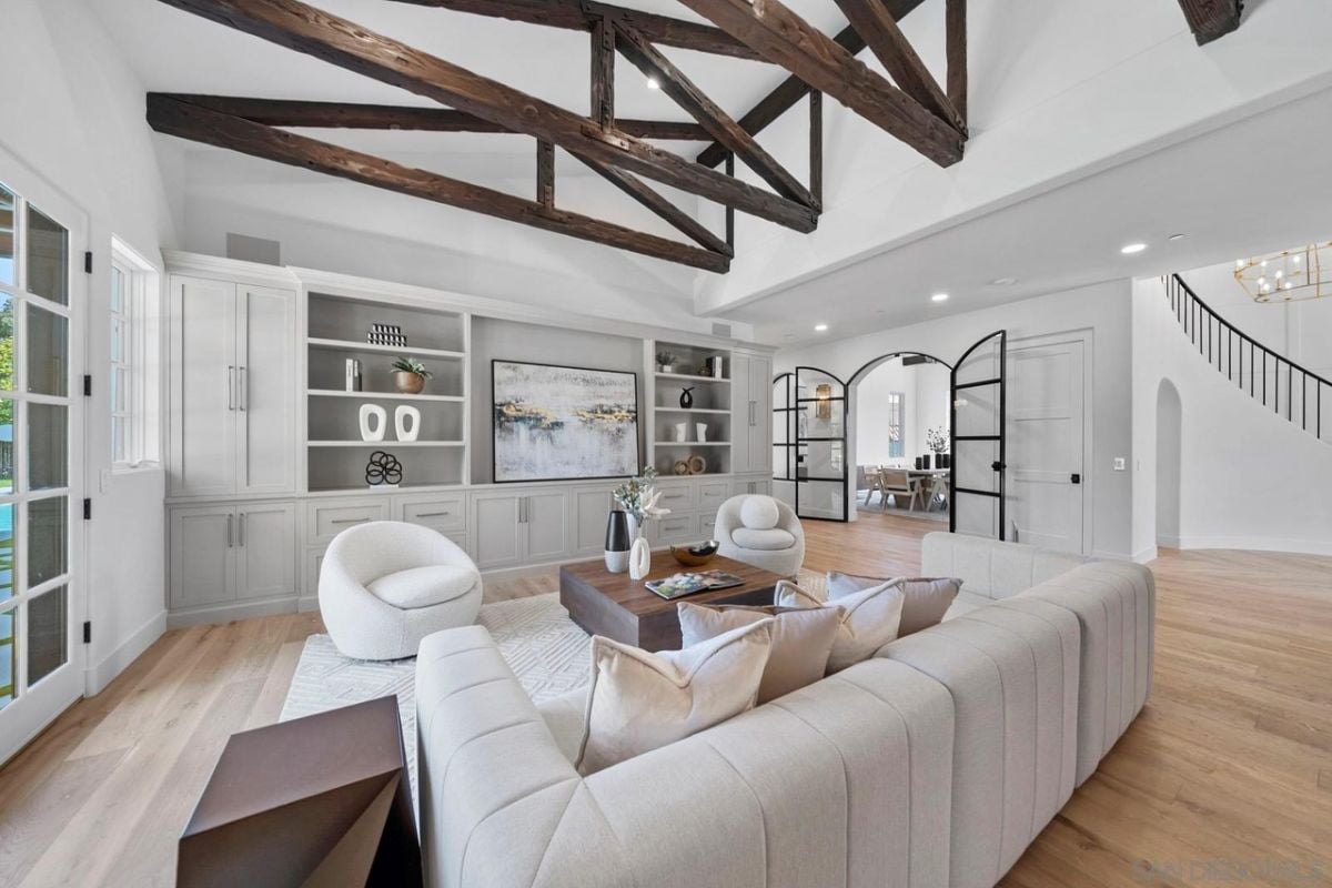 A living room with an exposed beam ceiling, cabinets, a TV, a couch, chairs, and a center table.