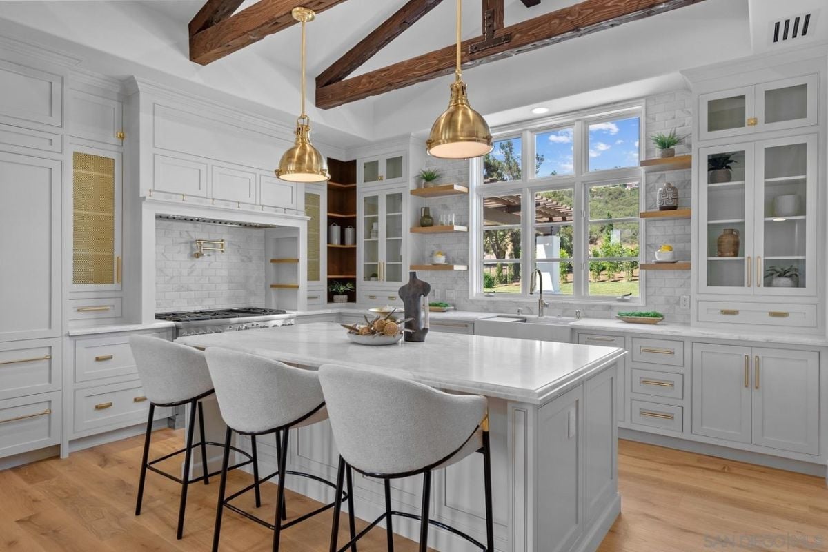 A kitchen with a center island, chairs, an exposed beam ceiling, countertops, cabinets, and a stove.