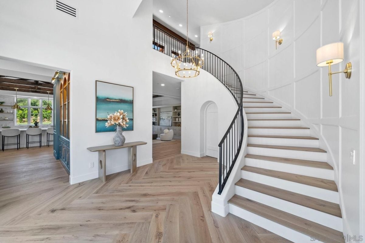 A foyer with a painting, a chandelier, and a staircase.