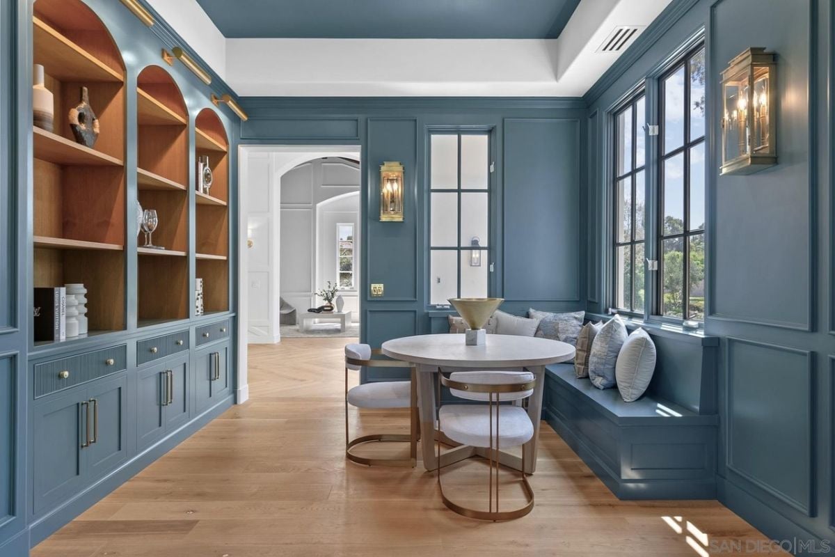 A breakfast nook with windows, cabinets, a shelf, a bench, and a round table with chairs.