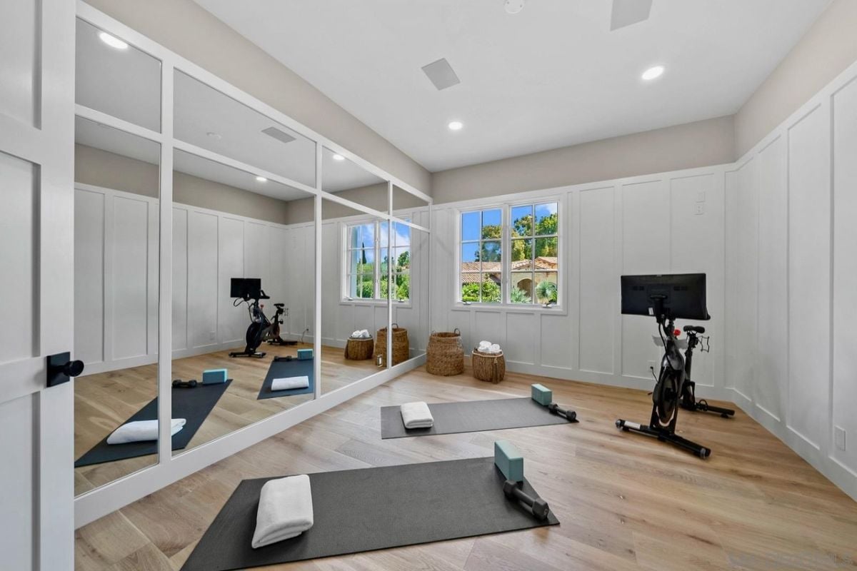 An exercise room with a window, a mirror, rugs, and a stationary bicycle.