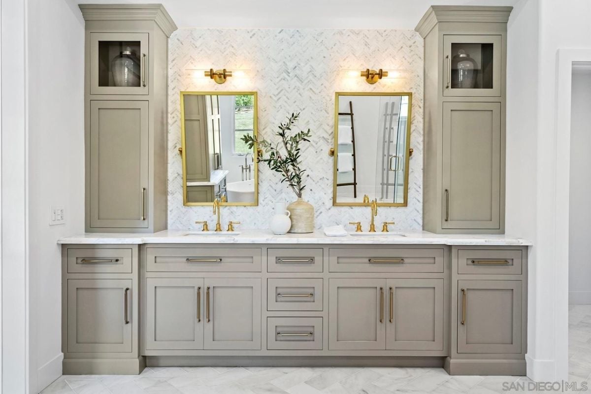 A bathroom with dual vanities, mirrors, and cabinets.