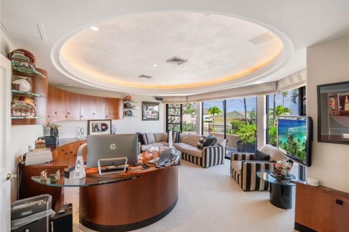 A home office with couches, windows, a TV, and a desk.