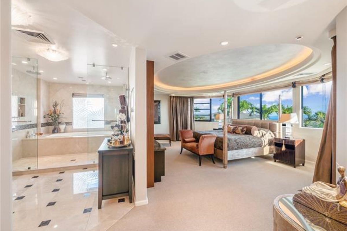 A bedroom with a canopy bed, windows, nightstand, couch, and attached bathroom.
