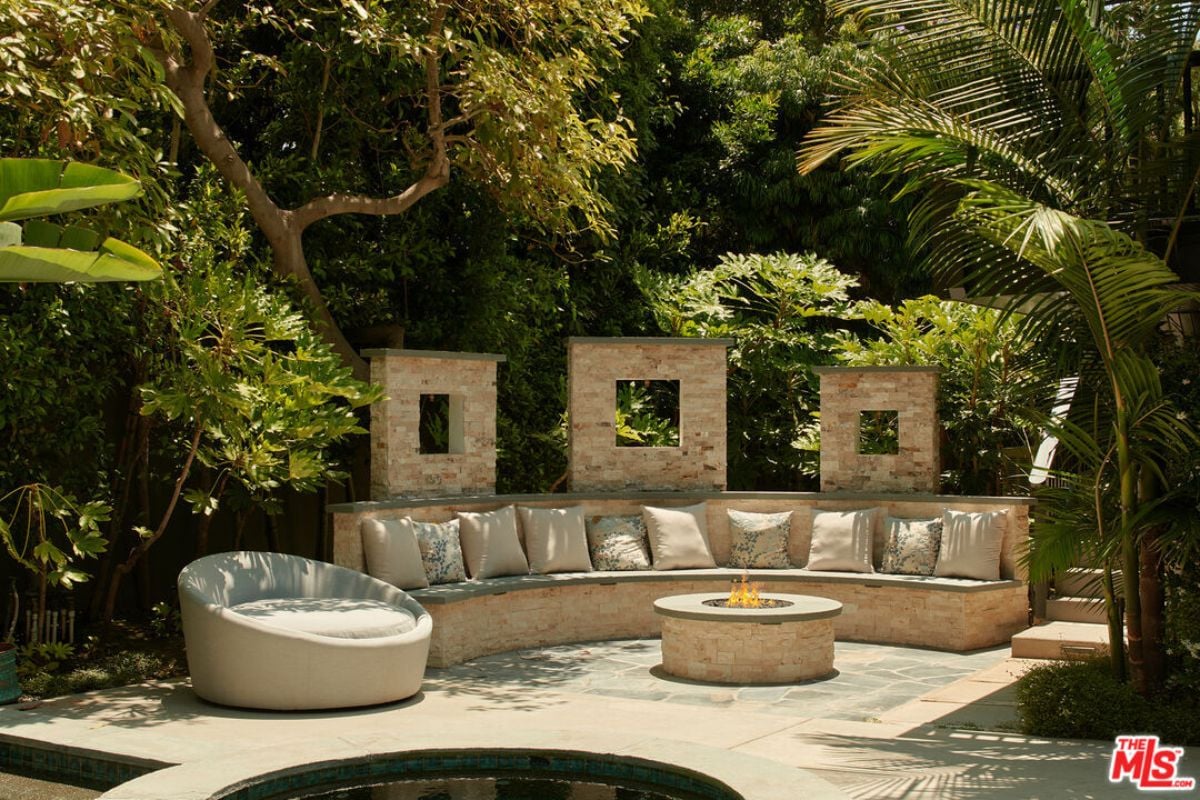 A patio with a stone bench, a comfy chair, and a firepit.