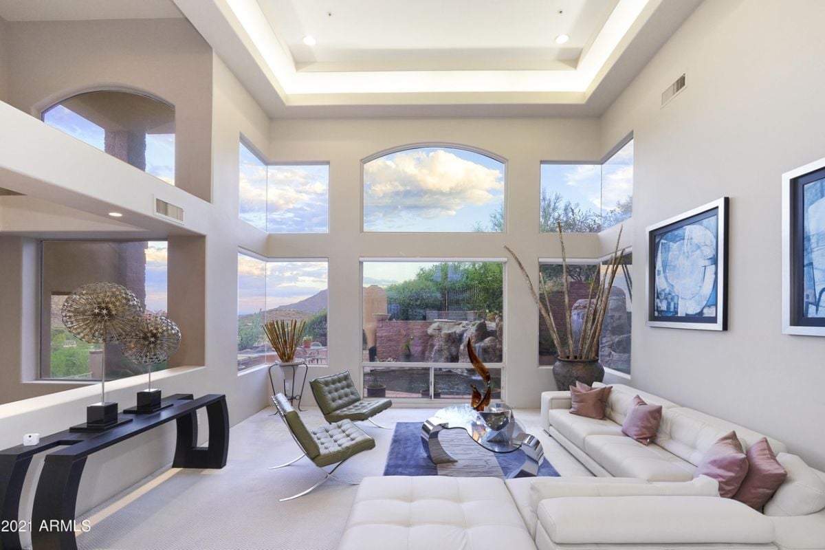 A living room with windows, paintings, a vase, chairs, a couch, and a center table.