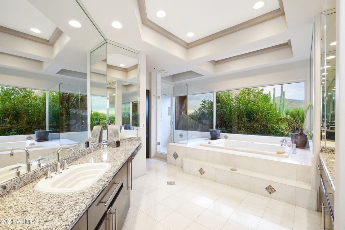 A bathroom with mirrors, windows, a vanity, and a bathtub.