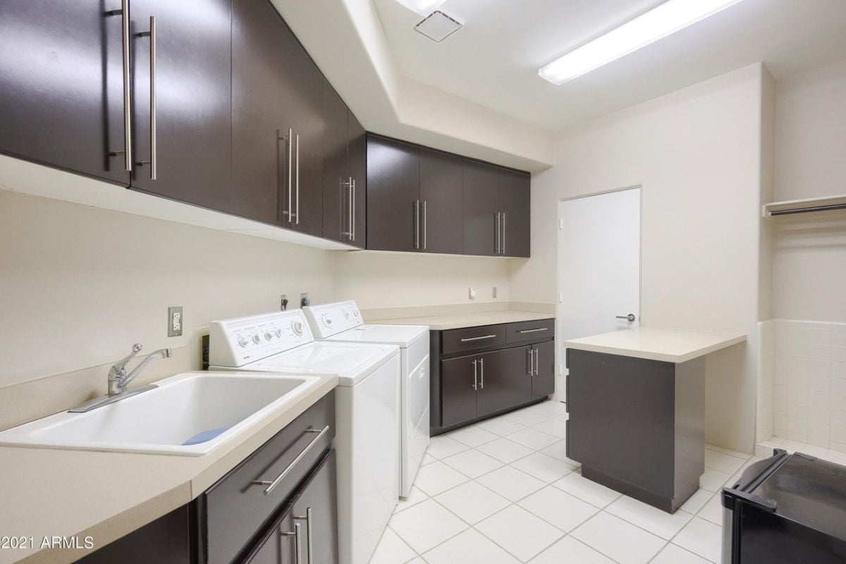 A laundry room with a sink, countertops, cabinets, and washing machines.