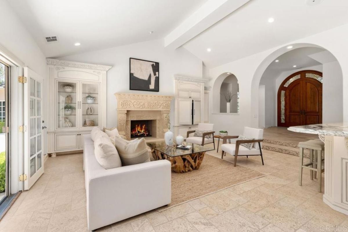 A living room with a painting, fireplace, cabinet, glass center table, chairs, and a couch.