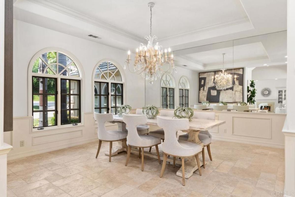 A dining room with a chandelier, windows, and a dining table surrounded by chairs.