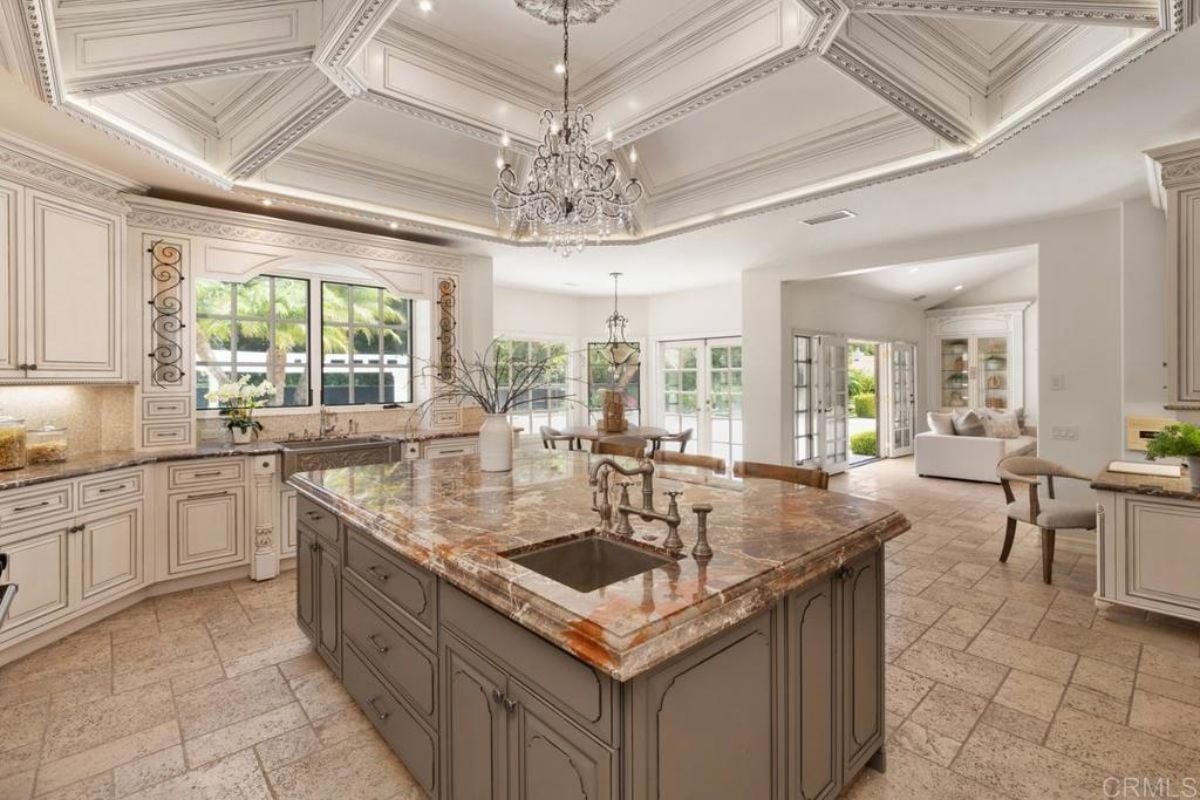 A kitchen with chandelier, countertop, island, cabinets, and kitchen appliances.