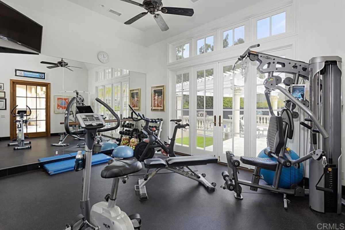A home gym with windows, a TV, a ceiling fan, and gym equipment.
