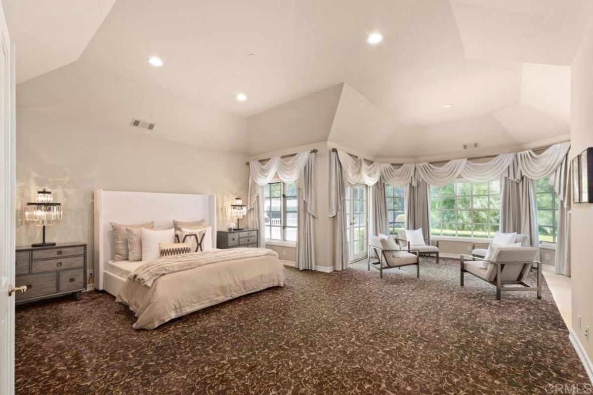 A bedroom with a bed, windows, chairs, a couch, and a nightstand.