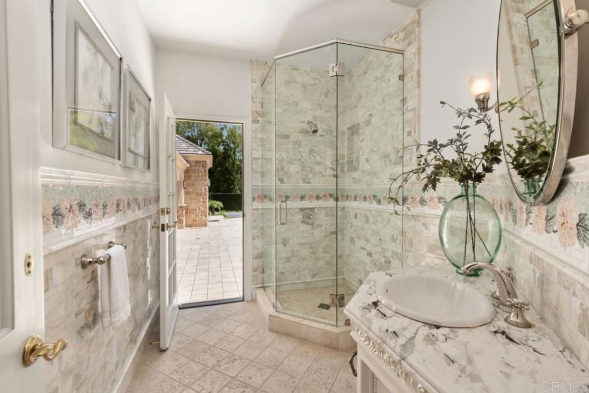 A bathroom with a vanity, mirror, and shower room.