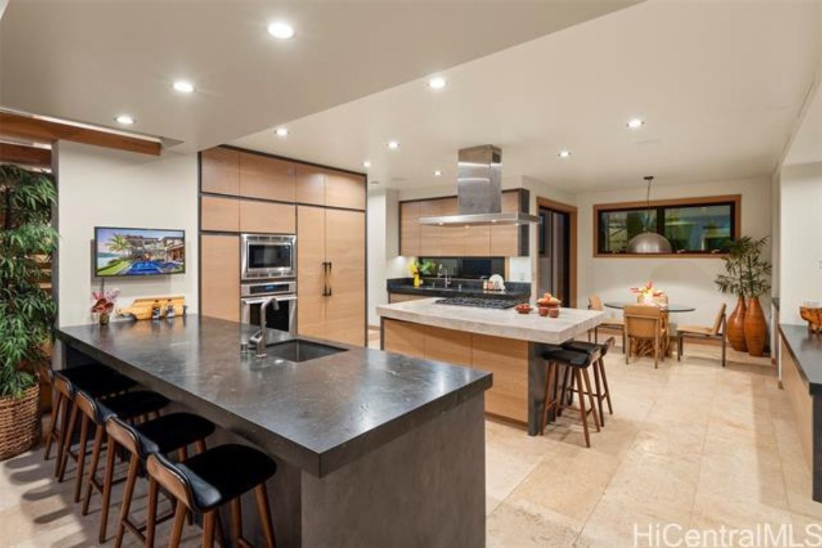 A kitchen with countertops, chairs, cabinets, and kitchen appliances.