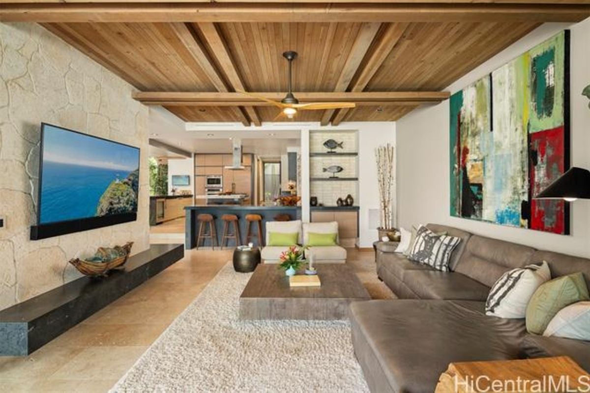A family room with a TV, exposed beam ceiling, rug, couch, center table, and bar.