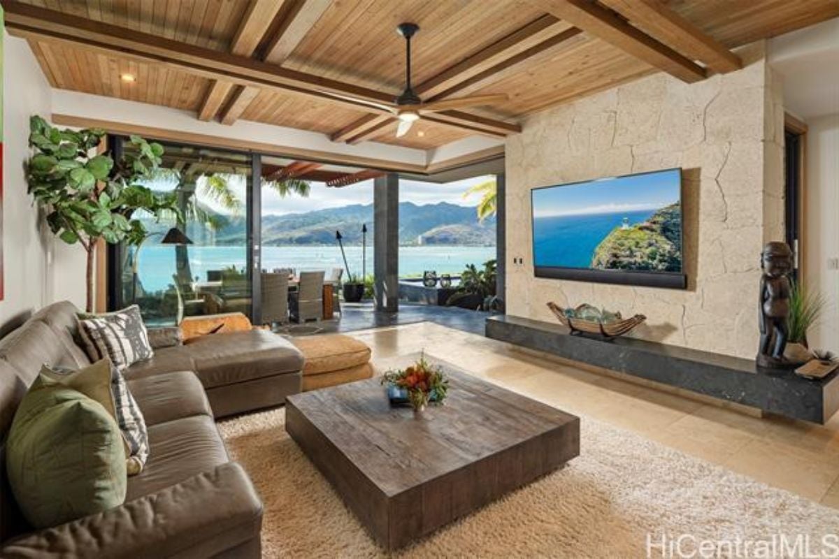 A family room with a TV, exposed beam ceiling, rug, couch, center table, and bar.