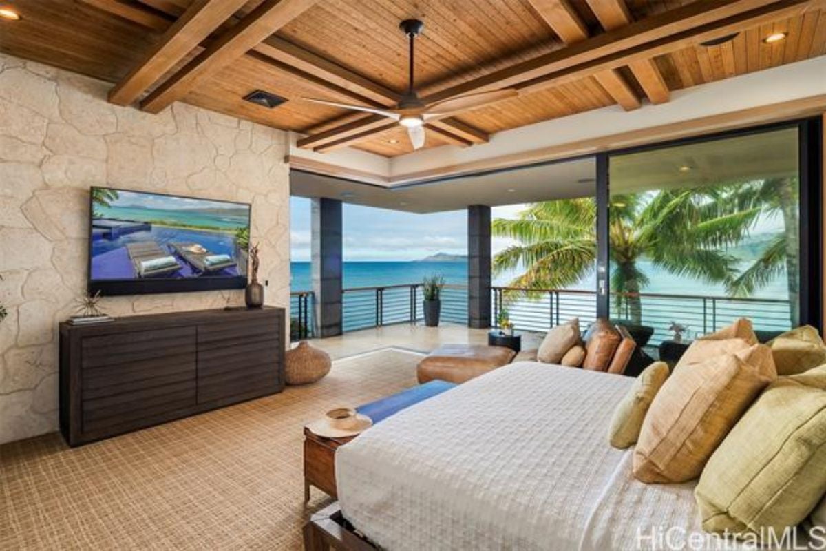 A bedroom with a bed, exposed beam ceiling, TV, cabinet, and ceiling fan.