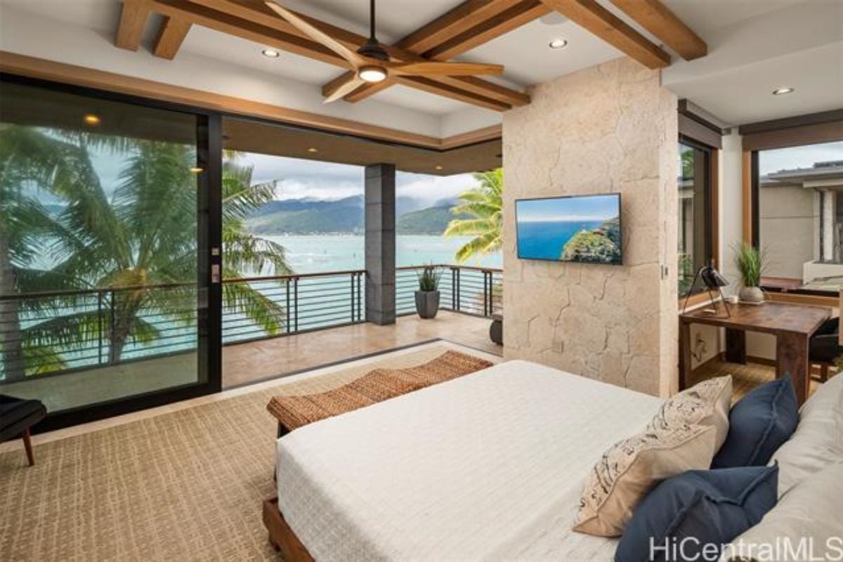 A bedroom with a bed, exposed beam ceiling, desk and ceiling fan.