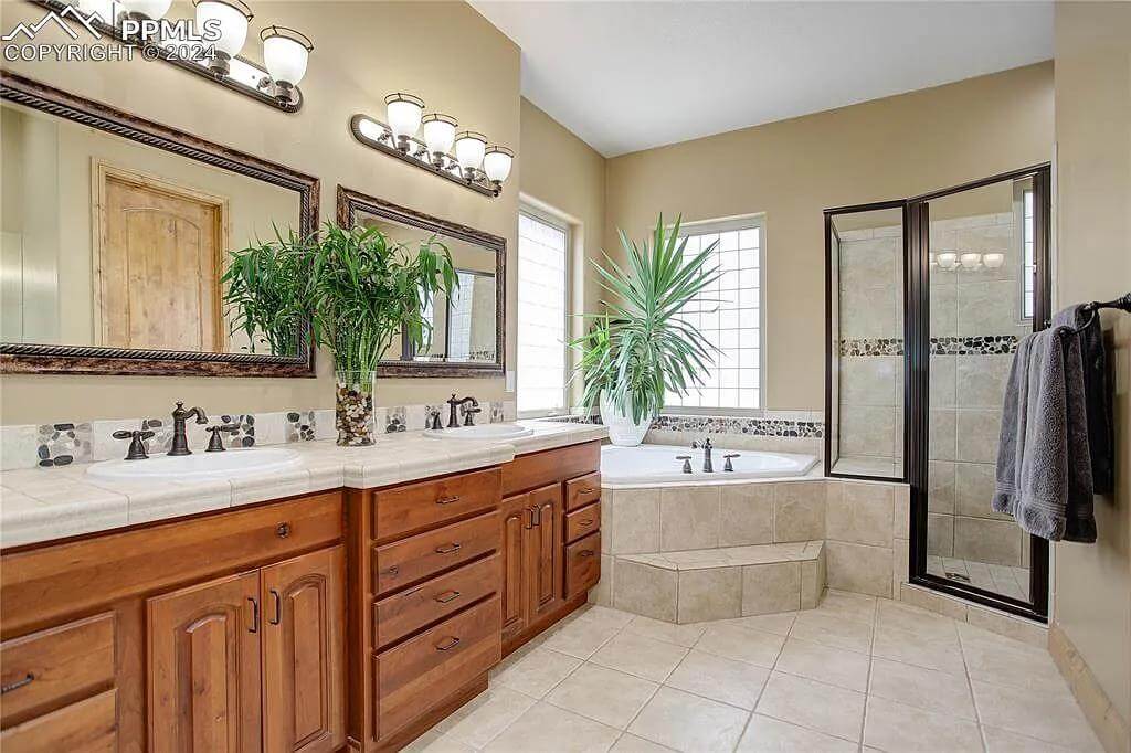 Primary bathroom with a dual sink vanity, a corner tub, and a tiled shower.