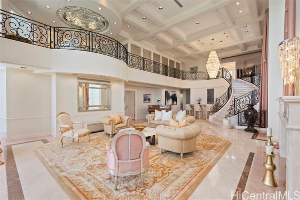 A living room with couches, chairs, a rug, a coffee table, tiled floor, a vase, and a staircase.
