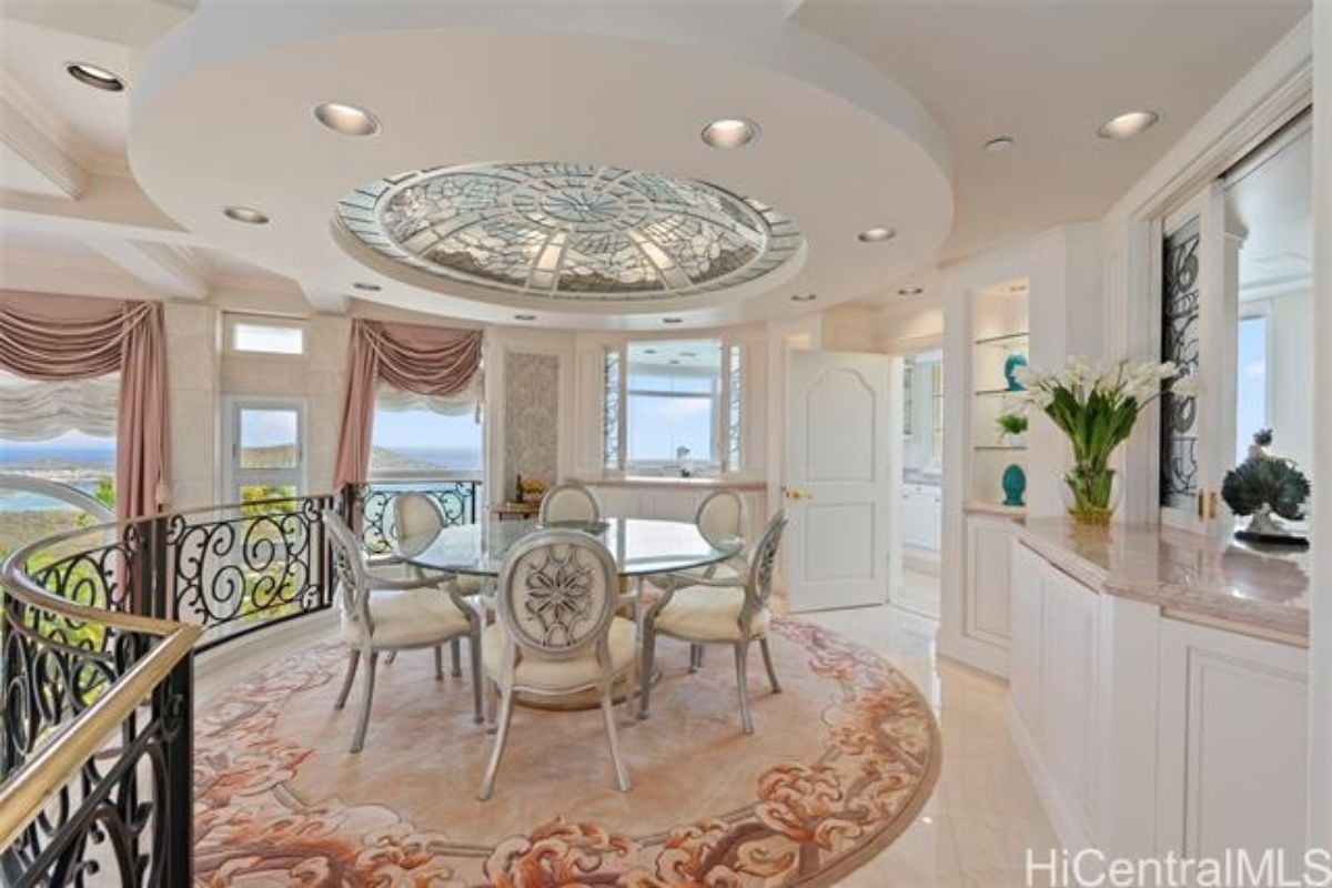A breakfast nook with a rug and a round glass dining table surrounded by chairs.