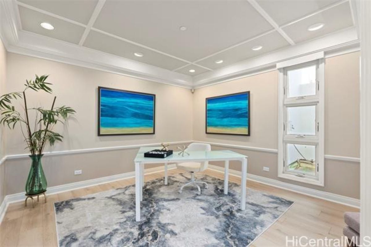 A home office with paintings, a rug, and a desk with a chair.