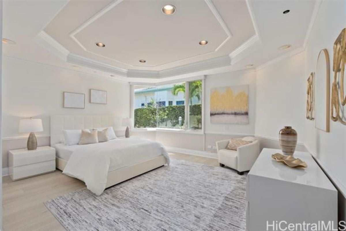 A bedroom with a bed, rug, nightstands, window, paintings, and a cabinet.