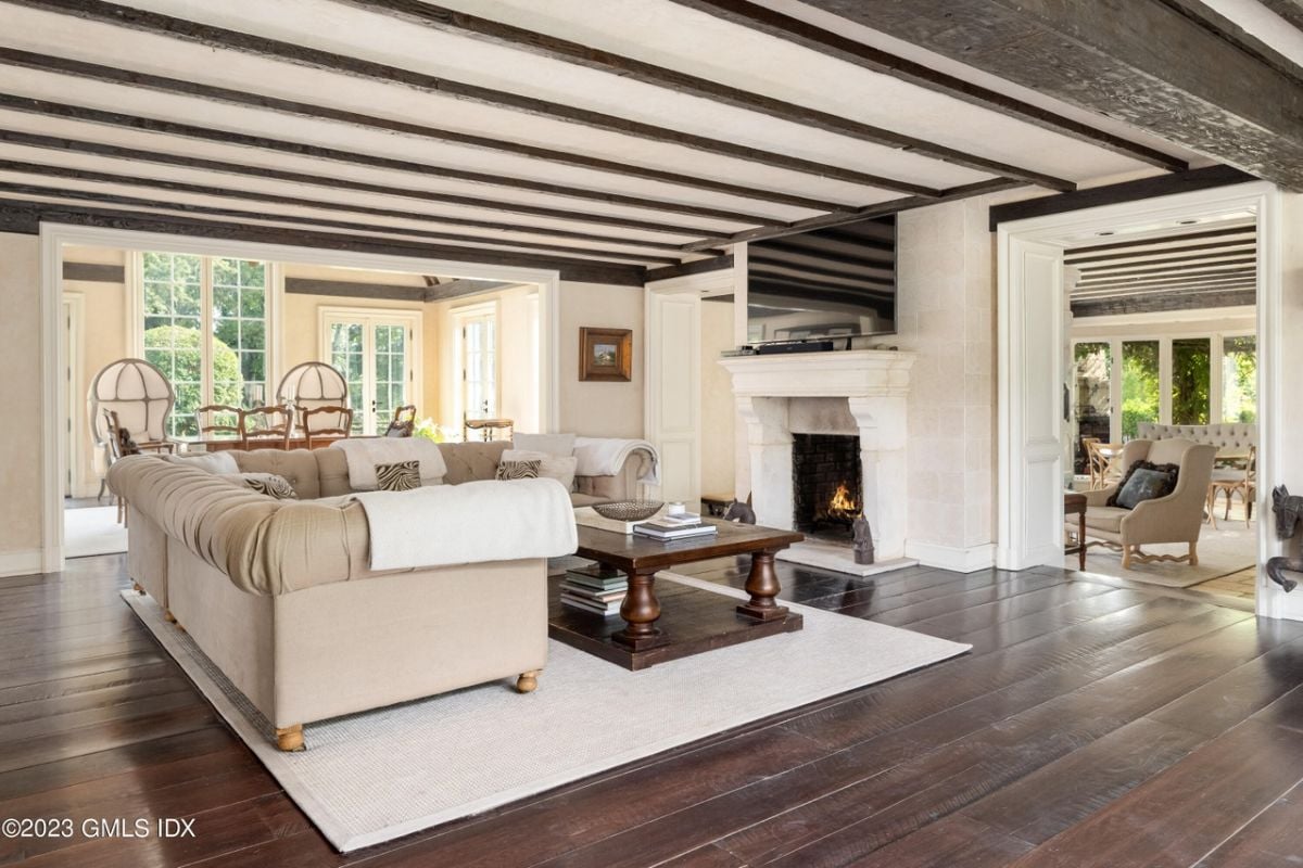 A living room with an exposed beam ceiling, wooden floor, TV, fireplace, rug, couch, and coffee table.