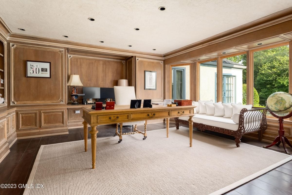 A home office with a window, a couch, a rug, cabinets, and a desk with an office chair.